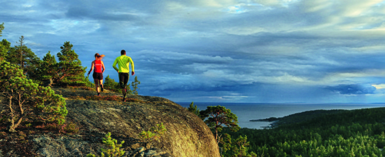 två personer, sedda bakifrån, springer över en bergskam med havet i bakgrunden