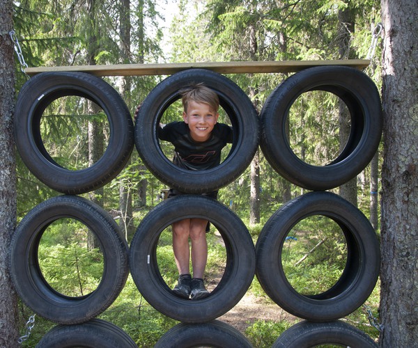 ett barn tittar ut genom en formation av bildäck i en skog