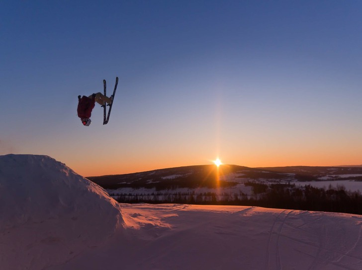 en skidåkare som gör ett hopp med en solnedgång i bakgrunden