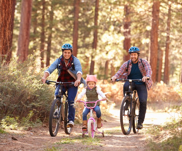 två vuxna och ett barn som cyklar i en skog