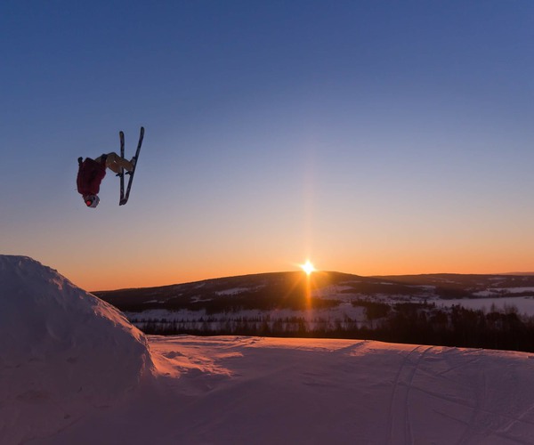 en skidåkare som gör ett hopp i luften med en solnedgång i bakgrunden