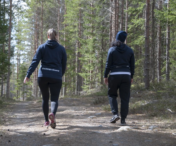 två personer, sedda bakifrån, vandrar på en stig i skogen