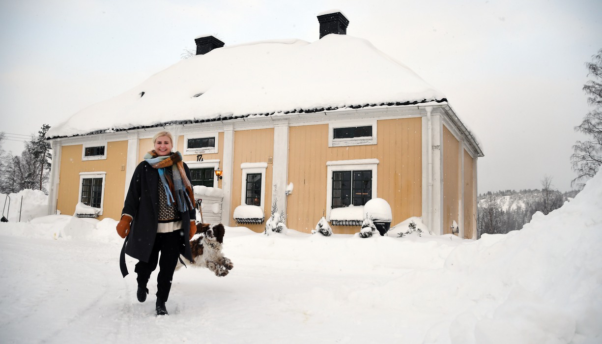 en kvinna och hennes hund tar en vinterpromenad utanför ett gult hus