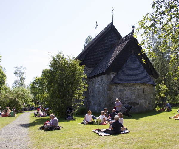 flera människor sitter i gräset utanför en gammal stenkyrka