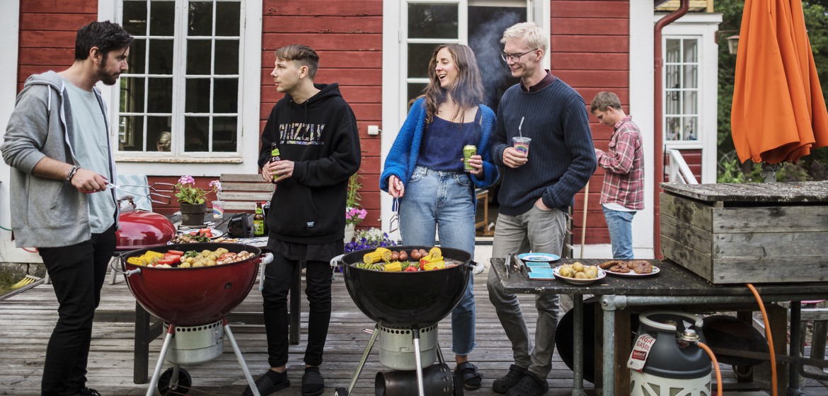 Tre killar och en tjej grillar framför en röd stuga på Äpplarö i Stockholms skärgård.