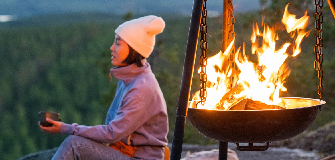 Kvinna sitter på ett berg vid en lägereld