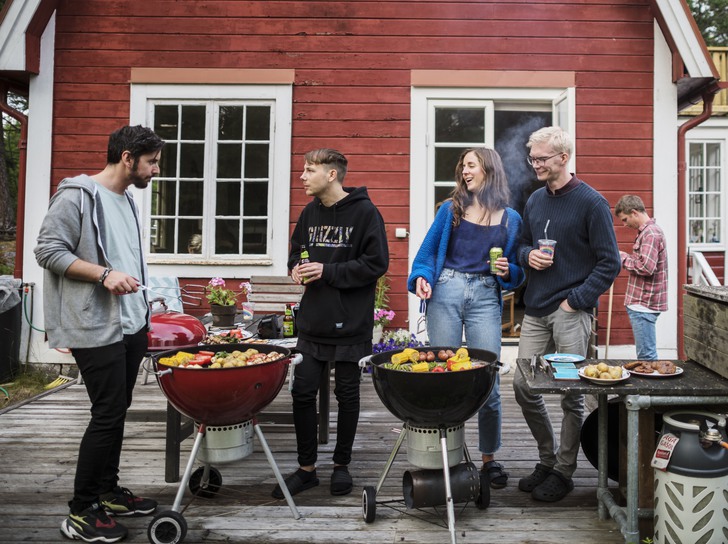 Tre killar och en tjej grillar framför en röd stuga på Äpplarö i Stockholms skärgård.