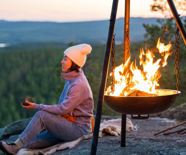 Kvinna sitter på ett berg vid en lägereld