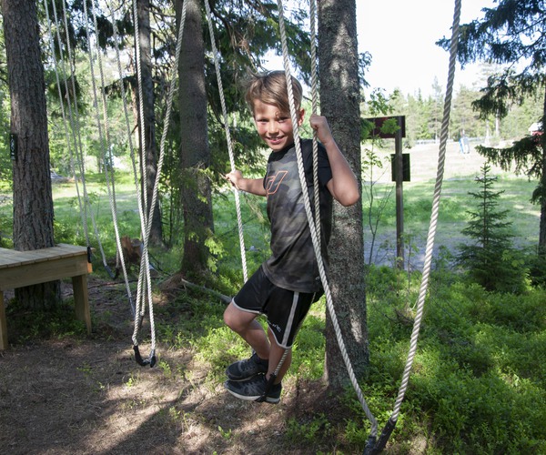 en pojke står i en repkonstruktion i skogen