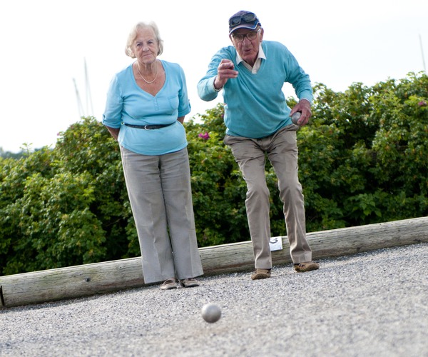 ett äldre par står på en grusbana. Mannen har just kastat ett bouleklot.