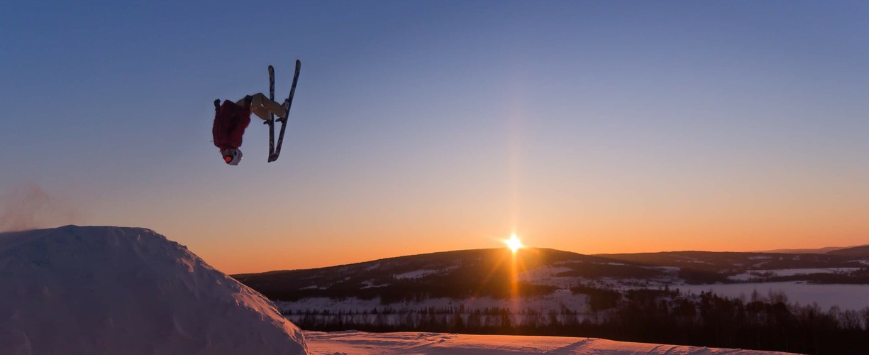 en skidåkare gör ett hopp i luften med en solnedgång i bakgrunden