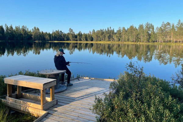 en ung person sitter på en brygga och fiskar i en sjö