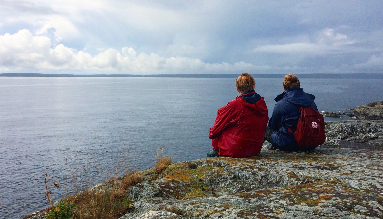 två personer sitter på en klippa och tittar ut över havet.