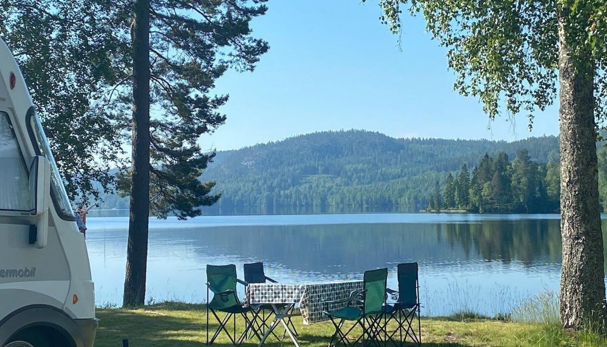 campingbord och campingstolar på en gräsmatta vid en sjö