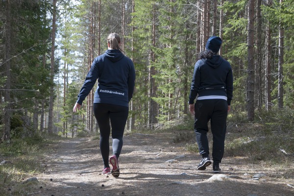 två personer, sedda bakifrån, vandrar på en stig i skogen