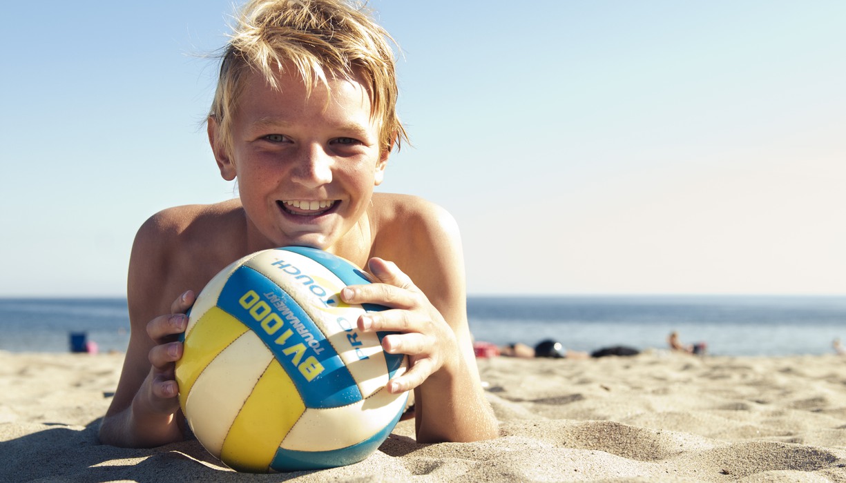 en pojke med en boll ligger på en sandstrand