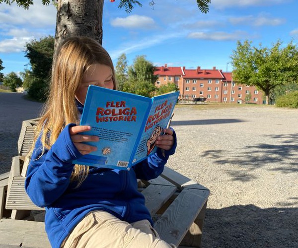 en flicka sitter på en bänk utomhus och läser en bok