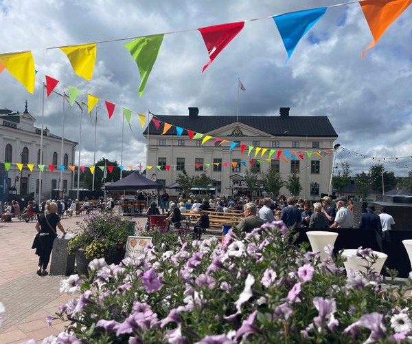 Ett torg med många människor. I förgrunden blommor.