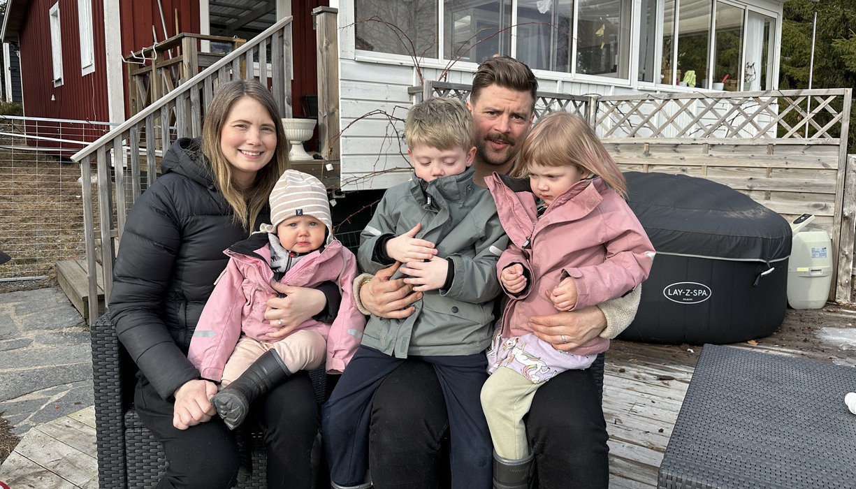 en familj med tre barn sitter utanför ett hus
