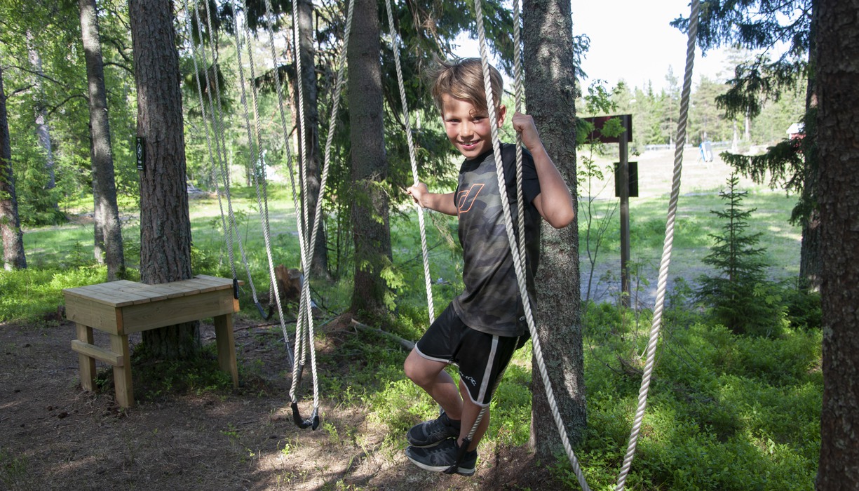 en pojke står i en repkonstruktion i skogen