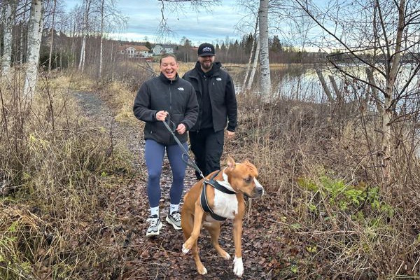 en kvinna och en man går med en hund på en stig nära vattnet