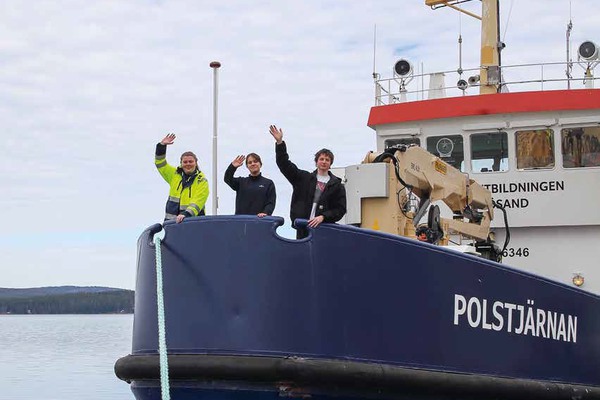 tre personer står på en båt och vinkar