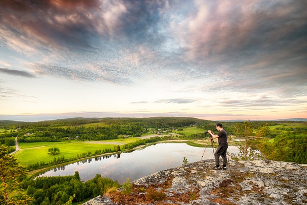 en person med kamera och stativ står på en bergstopp vid en sjö