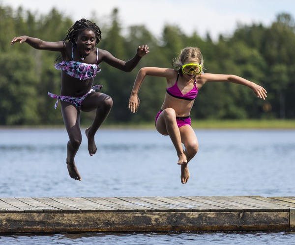 Flickor som hoppar i vattnet från en brygga.