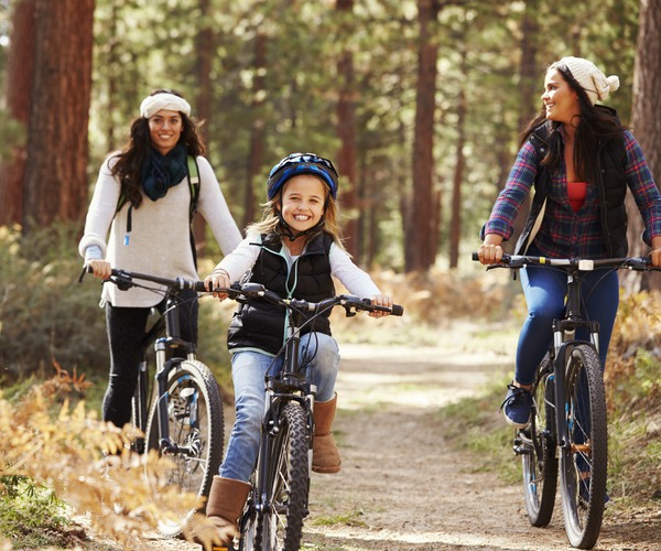 Två kvinnor och en flicka cyklar på en skogsväg.