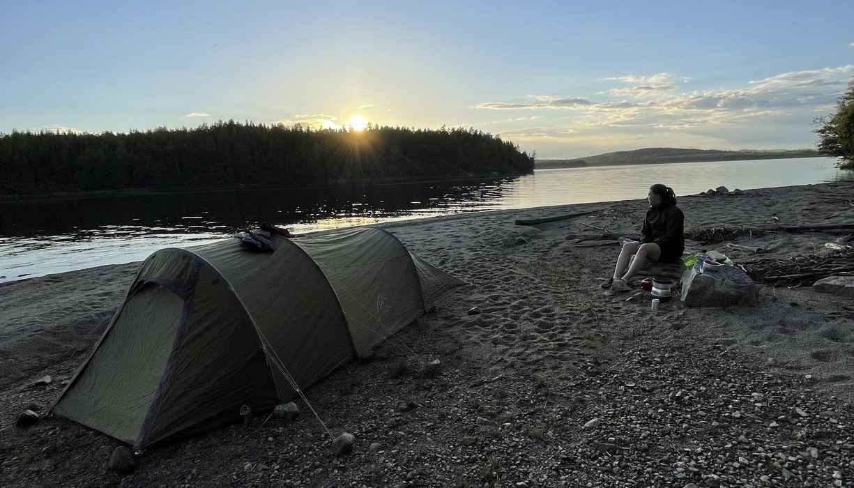 en person sitter vid ett tält på en strand i solnedgång