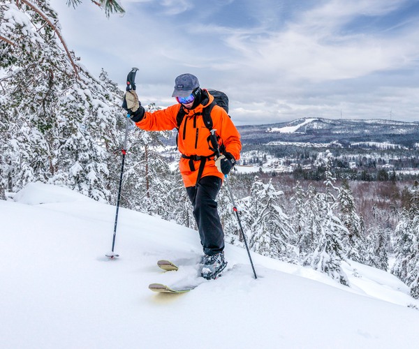 en person med orange jacka åker skidor uppför ett berg